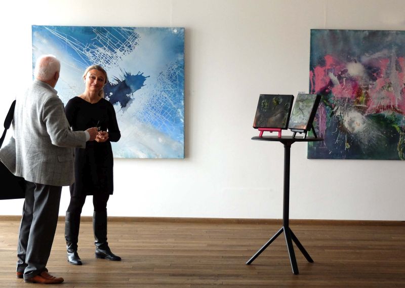 Cordula Rock im Gespräch mit einem Besucher vor den Bildern, die bei Jürgen Welker im Atelier entstanden sind