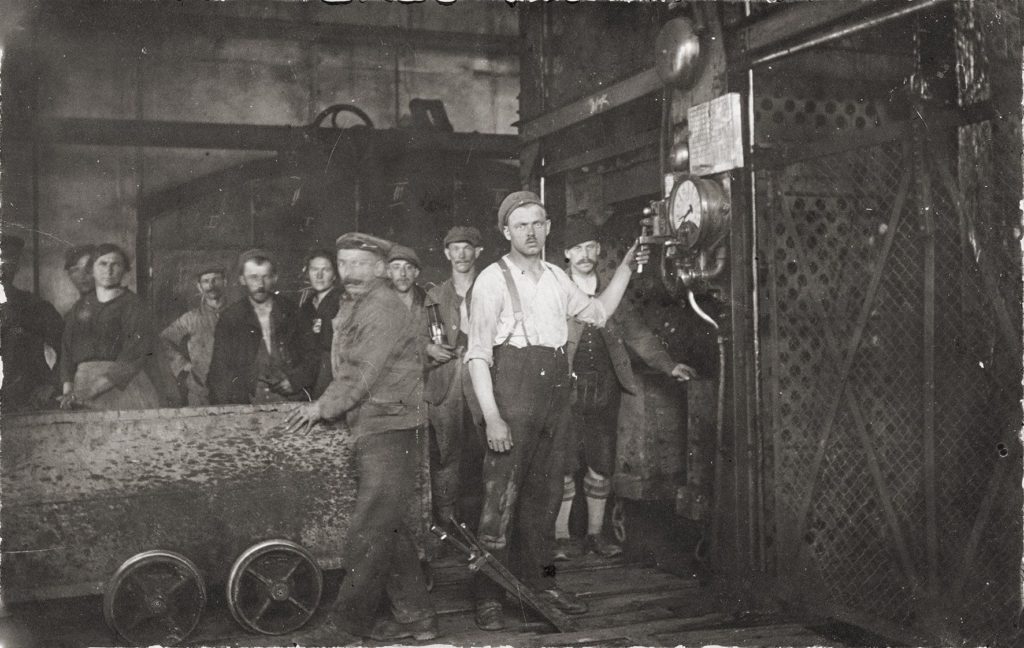 Bergleute um 1900 vor der Einfahrt in die Grube. In der Bildmitte steht der Anschläger, dessen Aufgabe war es, die Signalanlage zur Verständigung mit dem Maschinisten des F ö rderantriebes zu bedienen. Eine Ausrüstung, wi e Helme oder Schützer, gab es so gut wie gar nicht, erst nach dem Zweiten Weltkrieg wurde diese verpflichtend eingeführt.
